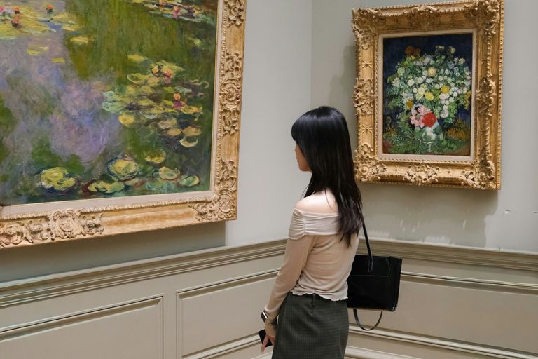 Mujer joven contemplando pinturas impresionistas enmarcadas en una sala de museo.
